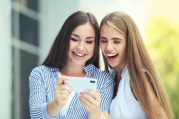 Two young happy girlfriends using mobile phone on the street