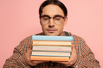 male nerd in eyeglasses with closed eyes holding books, Isolated on pink