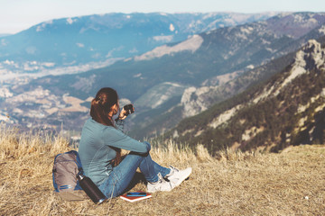 Fototapeta premium Young beautiful girl travels alone in the mountains in spring or autumn, sits on the edge of the mountain and looks into the distance and enjoys nature, rocks and green forests, view of the landscape