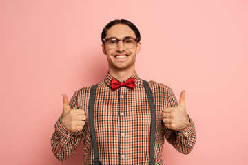 cheerful male nerd in eyeglasses showing thumbs up on pink