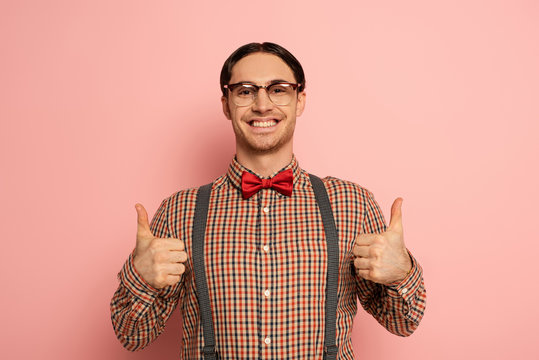 cheerful male nerd in eyeglasses showing thumbs up on pink