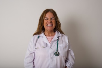 Mad crazy doctor woman clenches teeth angrily, being annoyed with coming noise, dressed in medical uniform, isolated over gray background. Negative feeling concept.