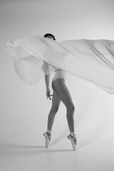 Ballerina in body on a white background in the studio with flying white fabric. Black and white video.