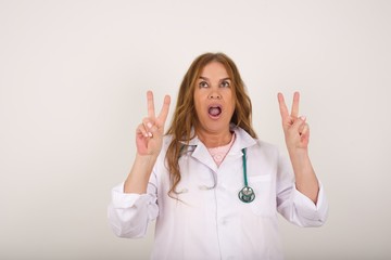 Isolated shot of cheerful European woman makes peace or victory sign with both hands, dressed in casual clothes, feels cool has toothy smile, isolated over gray background. People and body language.