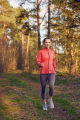 Healthy fit attractive young woman jogging in woodland along a forest track approaching the camera with a happy smile in an active lifestyle, health and fitness concept