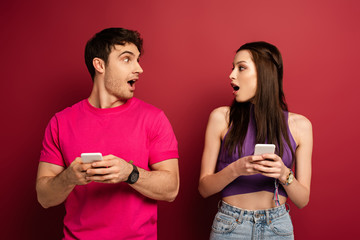 beautiful surprised couple using smartphones on red