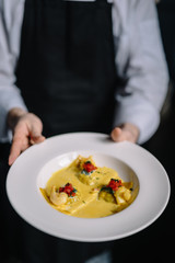 Chef of the restaurant holding on his hands plate of raviolli pasta with shrimps, salmon and curry sauce