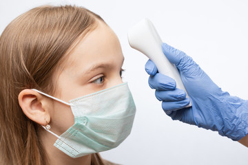 Doctor using infrared thermometer checking body temperature of girl wearing surgical mask -...