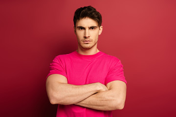 Fototapeta premium portrait of serious man with crossed arms in pink t-shirt on red
