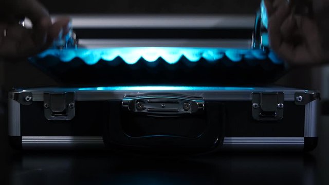 Secret suitcase with light. Concept. Close-up of woman opening mysterious black suitcase emitting neon light. Woman hides something unusual in mysterious suitcase