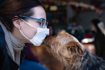 Living with coronavirus. Woman with mask kissing dog.
