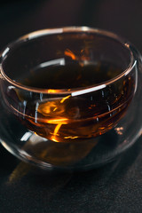 Transparent bowl with black tea on a wooden table. Bright flare of light in the drink. Vertical picture.