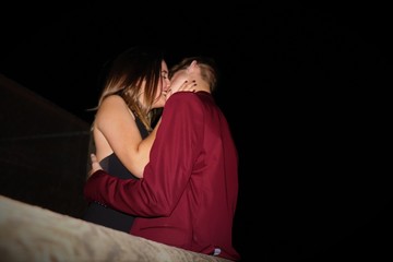 Pareja joven enamorada besándose de noche vestidos con americana roja y vestido negro