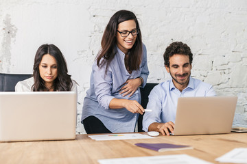 Young pregnant woman teaches two students working on the computer - Businesswoman during a...