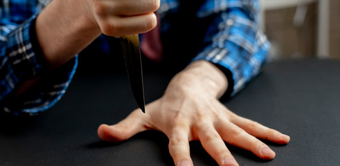 a hand with knife hitting between the fingers on the table, playing the game with a sharp blade wide web banner