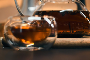 Transparent teapot with black tea on a wooden table. Bowl in the foreground