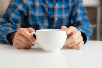 person sitting at the table and drink cup of tea at home in the evening
