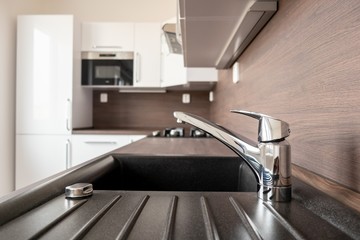 Chrome faucet in a brand new kitchen with blurred background with microwave oven and fridge in a...