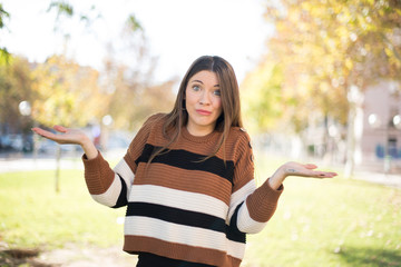 Naklejka premium Puzzled and clueless young woman with arms out, shrugging her shoulders, saying: who cares, so what, I don't know. Negative human emotions, facial expressions, life perception and attitude.