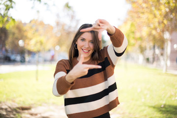 Portrait of young blonde positive female with cheerful expression, dressed in casual light blue sweater, has good mood, gestures finger frame actively at camera.