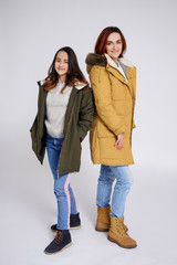 portrait of smiling mother and daughter in warm clothes posing over grey © Di Studio