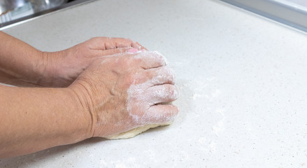 Hands of granny kneads dough. 60 years old woman hands kneading dough. Grandmother dough molding on table. Wheat homemade baking. Pastry and cookery.