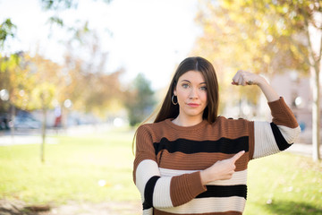 Naklejka premium Waist up shot of blonde woman raises hand to show her muscles, feels confident in victory, looks strong and independent, smiles positively at camera, stands against gray background. Sport concept.