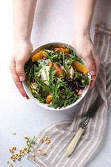 Healthy food. Fresh salad with arugula, mozzarella, baked beetroot, oranges and pine nuts in the bowl with hands. Background image, copy space
