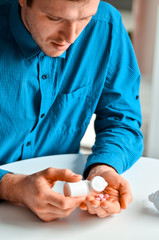 Young businessman in blue shirt holding a jar with a pills at the table at home