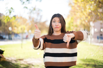 Pretty young pensive woman making good-bad sign. Displeased and unimpressed wearing casual clothes.