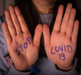 The hands of a caucasian person making the stop gesture. Stop covid19 written on the hands