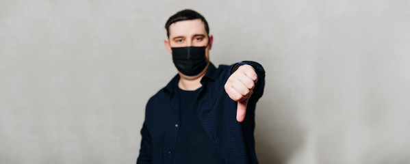 man in black shirt and black hospital mask on gray wall background