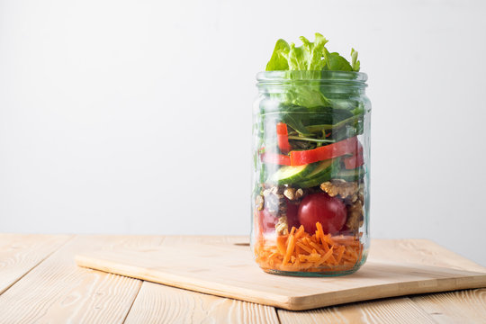 Healthy homemade mason jar salad with fresh pear tomatoes, carrots and herbs. Vegetarian concept.