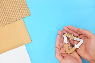 Hands holding a recycling symbol made of paper cardboard in blue background. Top view, reduce, reuse, recycle.