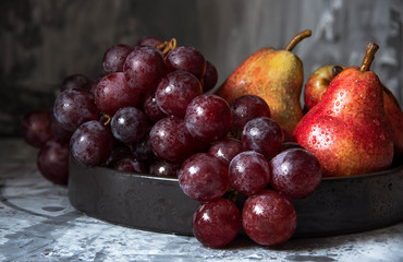 bunch of purple grapes and ripe pear fruits on dark plate, no people