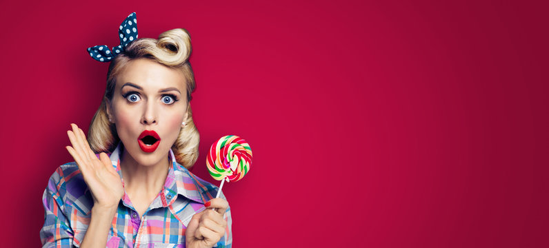 Excited woman with lollipop. Girl pin up with open mouth. Blond model at retro fashion and vintage concept. Dark red color background. Copy space for some text . Wide horizontal banner composition.