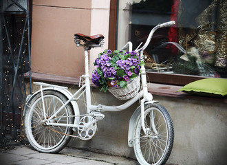 Fototapeta na wymiar White bycicle with flower basket near shop