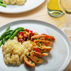 Two plates with baked chicken fillet, potato, green beans and vegetable sauce. Delicious meal with wine on a wooden table. Traditional healthy lunch for two people.