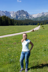 Obraz premium Caucasian teenage girl with glasses on a green meadow at the foot of the mountain, Montenegro.