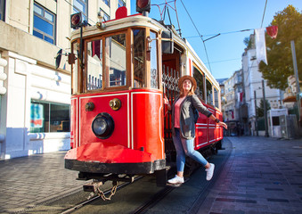 Beautiful young girl tourist in a hat poses in front of tram at popular Istiklal street in Beyoglu,...