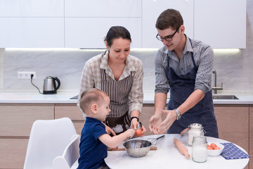 Mother, father and son are preparing dough for the cookies in the kitchen. Fun family tradition to cook together. Caring for loved ones. Modern lifestyle in home.