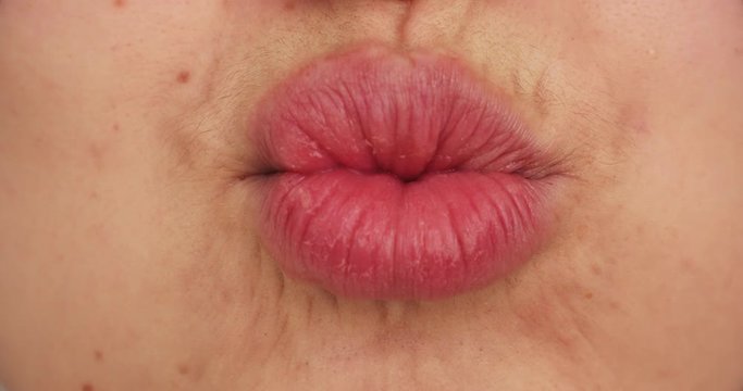 Close-up of unrecognizable woman with plump lips with lipstick making a kiss at camera and smiling.