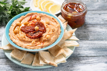 A bowl of creamy homemade hummus with with sun-dried tomatoes, olive oil and pita chips. traditional vegan healthy meal