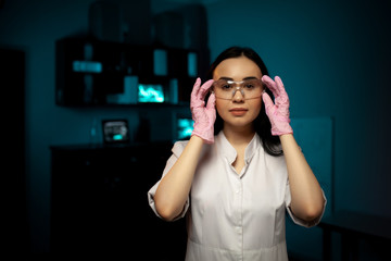 Portrait of confident professional female doctor standing in hospital room putting glasses on....