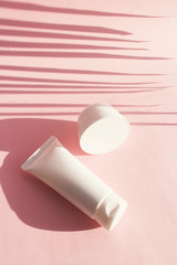 A tube of cosmetics with a shadow from a palm leaf. The concept of minimalism cosmetic packaging. Layout for branding, labels and packaging.