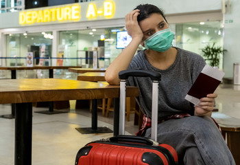 Distraught, stressed girl traveler with a medical mask on her face is waiting for missed, delayed...