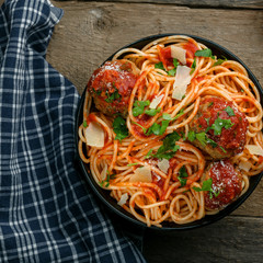 Traditional Italian spaghetti with meatballs and parmesan in tomato sauce in a black bowl. American family meal on a table. Top view shot.
