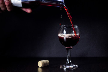 Red wine pouring from the bottle to the glass with splashes on black background