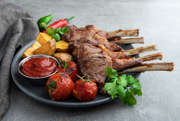 Roasted rack lamb chops on a plate with red sauce potatoes and tomatoes