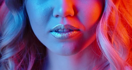 Closeup shot of face of girl wearing glowing makeup doing a seductive growl in neon light - nightlife concept 4k footage
